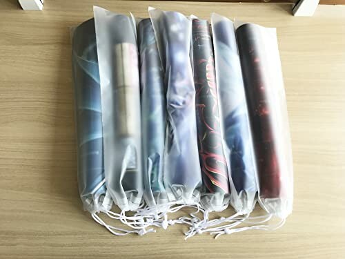 Six rolled posters in fabric bags on a wooden surface.